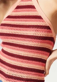Inquadratura ravvicinata di un top senza maniche in maglia con strisce orizzontali nei toni del rosa e del bordeaux su un torso superiore di una persona.