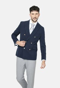 Blazer navy de doble botonadura con botones metálicos, solapas de muesca y pantalones ajustados grises. Tejido ligero y textura suave.