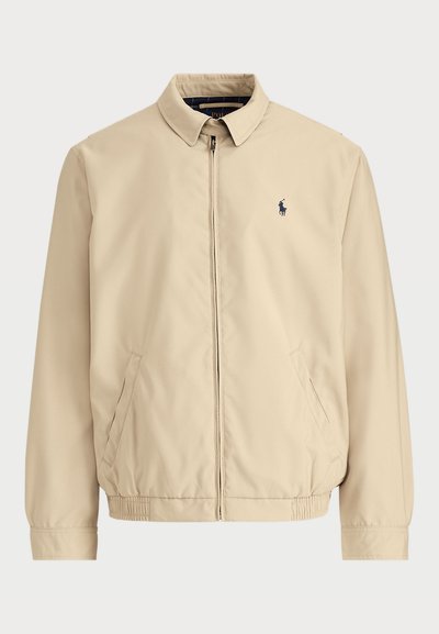 Μπεζ ελαφρύ μπουφάν με όρθιο γιακά, μπροστινό φερμουάρ, πλαϊνές τσέπες και μικρό ναυτικό λογότυπο στο αριστερό στήθος. Κατασκευασμένο από λείο ύφασμα.