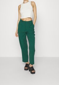 Zelené kalhoty s vysokým pasem a mírně volným střihem, s velkými knoflíky a kapsami. Spárovány s bílým zkráceným topem a černými platformovými botami.