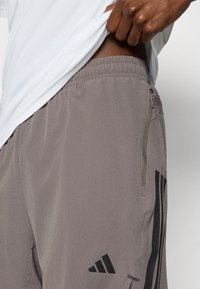 Γκρι αθλητικό σορτς από ελαφρύ, υφασμάτινο με υφή, με πλαϊνή τσέπη με φερμουάρ και μαύρες ρίγες ως διακοσμητικά στοιχεία.