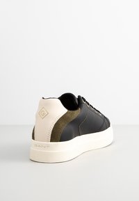 Baskets en cuir noir avec semelle blanche, détail en daim olive et languette beige au talon avec logo "G", vues de l'arrière côté droit.