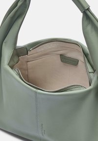 Zielona skórzana torebka z zamkiem błyskawicznym na górze, miękka w dotyku, z beżowym wnętrzem. Posiada metkę i pojedynczy uchwyt do noszenia.