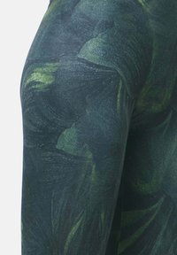 Leggings z navadnim temnozelenim in teksturiranim vzorcem z valovitimi oblikami. Narejene iz raztegljive tkanine, ki poudarja udobje in fleksibilnost.