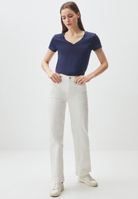 Top corto navy a v con maniche corte abbinato a pantaloni bianchi a vita alta e scarpe da ginnastica bianche. Tessuto morbido con una texture liscia.