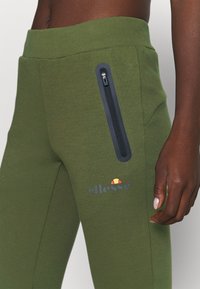 Grønne sweatpants med en sidelomme med lynlås, elastisk talje og et lille broderet logo. Glat tekstur med tætsiddende design.