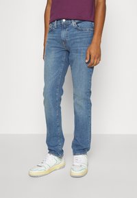 Ljust blå denimjeans med rak passform, femfickorsdesign och subtila blekningar. Bärs med vita sneakers med färgglada detaljer.