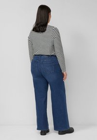 Niebieskie dżinsy o szerokich nogawkach i prostym kroju, z dwoma tylnymi kieszeniami i gładką fakturą denimu. Sparowane z czarno-białą, paskowaną bluzką z długim rękawem.