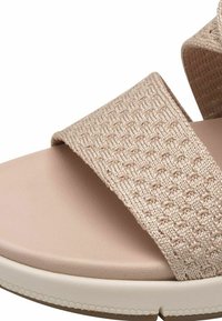 Beige Sandale mit einem strukturierten, gewebten Riemen und einer glatten, geformten Fußbett mit einer weißen gummiähnlichen Sohle, die für Komfort und Stabilität ausgelegt ist.