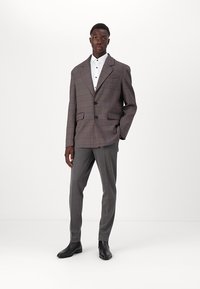 Rutet blazer i grått, rødt og blått med notched lapels, to knapper og sidelommer, paret med grå bukser og svarte støvler.