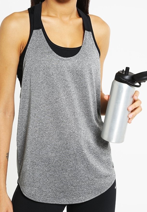 Femme en haut de sport gris sans manches tenant une bouteille d'eau argentée avec un bouchon noir sur fond blanc.