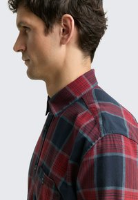 Rotes und marineblaues Flanellhemd mit Karomuster, Button-Down-Kragen und Brusttasche. Verfügt über einen strukturierten Stoff und eine taillierte Silhouette.