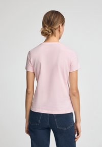 Kurzärmliges, hellrosa Baumwoll-T-Shirt mit rundem Ausschnitt. Einfaches Design, glatte Textur und klassischer Schnitt. Getragen mit blauen Denim-Jeans.