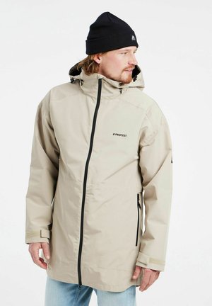 Giacca impermeabile beige con cappuccio, zip nera e tasche laterali. Presenta polsini regolabili e un logo discreto sul petto.