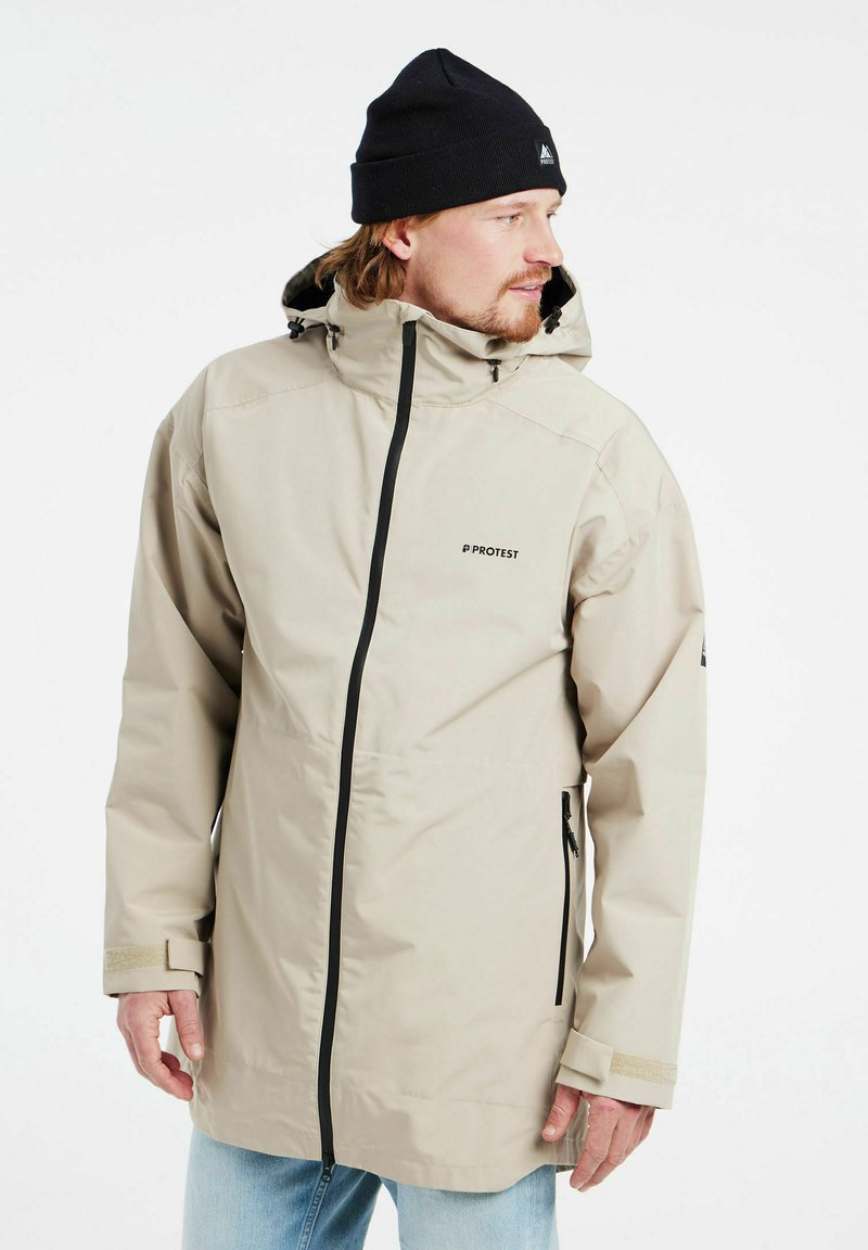 Giacca impermeabile beige con cappuccio, zip nera e tasche laterali. Presenta polsini regolabili e un logo discreto sul petto.