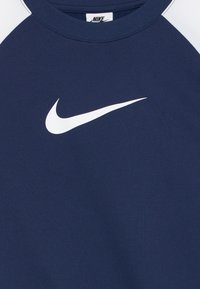 T-shirt de sport bleu foncé avec des manches blanches et un logo swoosh blanc centré sous le col rond.