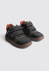 Zapatos negros y marrones con dos tiras de velcro, suelas de goma y un interior naranja contrastante. Presentan costuras y una parte superior texturizada.