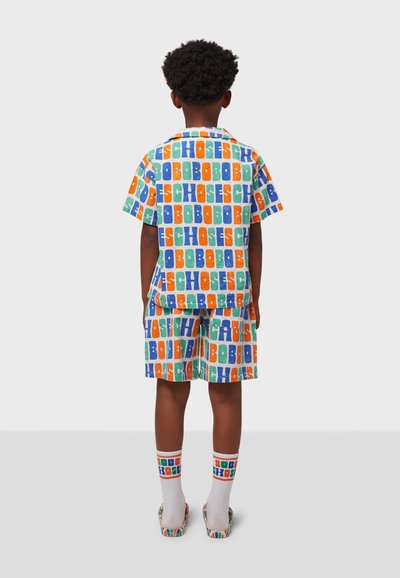 Ensemble de pyjama pour enfants avec des manches courtes et un short, présentant un motif coloré en lettres block dans des teintes d'orange, de bleu, de vert et de blanc.
