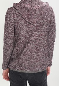 Sweat à capuche en maille bordeaux et gris avec un cordon de serrage, tissu texturé, manches longues et coupe décontractée. Vue de dos montrant les détails des coutures.