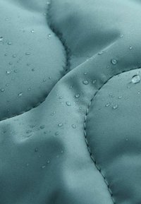 Gros plan sur un tissu matelassé bleu-vert avec des gouttes d'eau éparpillées sur sa surface texturée.