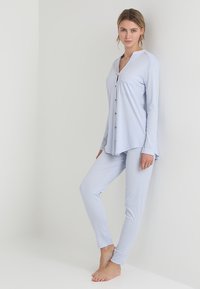 Světle modrý pyžamový set skládající se z košile s dlouhým rukávem na knoflíky s kapsou a odpovídajících slim-fit kalhot, vyrobený z měkké, hladké látky.