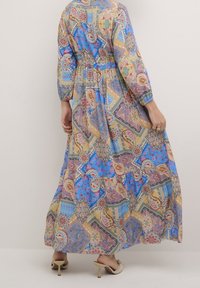 Maxi kjole i blå med et mosaikmønster, der inkluderer paisley- og geometriske designs. Lange ærmer og samlet talje, lavet af letvægtsstof.