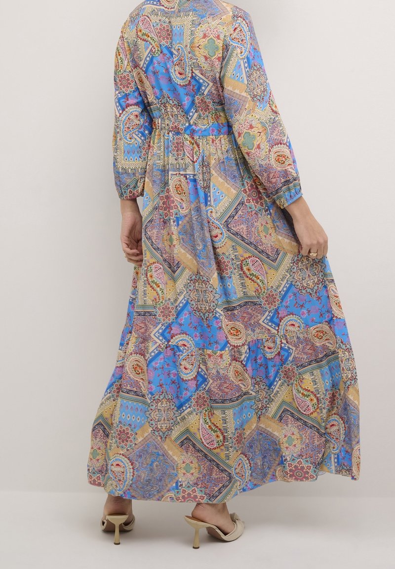Maxi kjole i blå med et mosaikmønster, der inkluderer paisley- og geometriske designs. Lange ærmer og samlet talje, lavet af letvægtsstof.