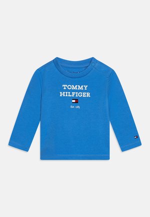 Blå langærmet toddler-skjorte med teksten "Tommy Hilfiger", logo og "Est. 1985" centreret foran, med trykknapper på den ene skulder.