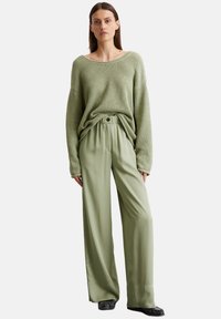 Olive green knitted sweater with a wide neckline, paired with lightweight, loose-fitting olive green pants featuring an elastic waistband and button.