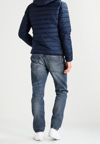 Námořnická prošívaná bunda s horizontálním prošíváním, doplněná o světle modré džíny. Bílé tenisky dokončují outfit.