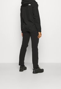 Czarna wodoodporna kurtka z kapturem, z elastycznymi mankietami i logo North Face. Do tego dopasowane czarne spodnie i czarne buty sportowe.