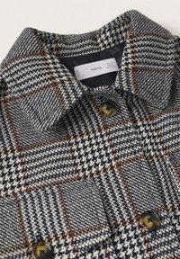 Col et boutons d'une veste à motif pied-de-poule gris, noir et marron avec une étiquette de marque MNG visible.