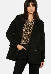 Schwarzer Peacoat aus Wollmischung mit weiterem Kragen, doppelreihigen Knöpfen und Seitentaschen. Kombiniert mit einer Bluse mit Leopardenmuster und schwarzer Hose.