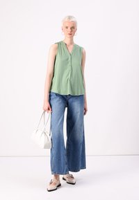 Lys grønn ermeløs bluse med knappedetaljer, kombinert med vide blå denimjeans. Hvit veske og lyseflate sko.