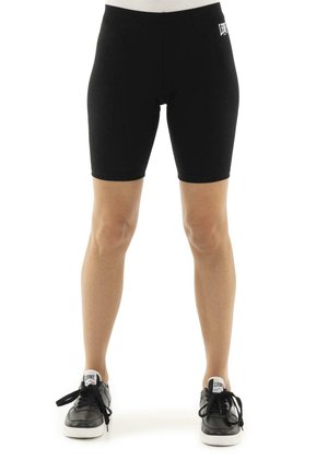 Vue de face d’un modèle portant un short de cyclisme noir et des baskets noires sur fond blanc.