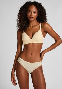 Gelbes, geripptes Dessous-Set mit einem BH mit Spitzenbesatz und Schleife, kombiniert mit Spitzen-Akzentuierter Slip. Weiche Textur, zarte Details.