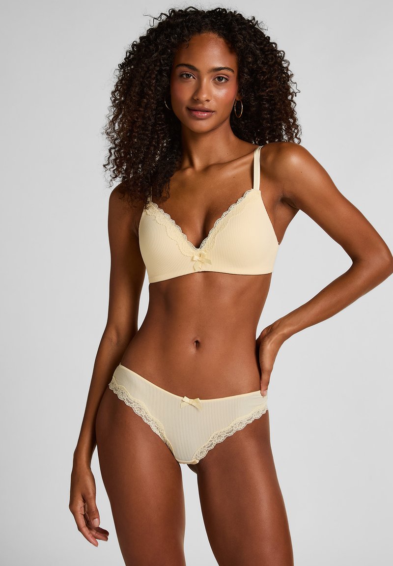Gelbes, geripptes Dessous-Set mit einem BH mit Spitzenbesatz und Schleife, kombiniert mit Spitzen-Akzentuierter Slip. Weiche Textur, zarte Details.