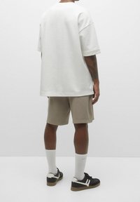 T-shirt oversized en coton blanc, short beige court, baskets noires avec accents blancs et chaussettes de sport blanches. Design minimaliste, coupe décontractée.