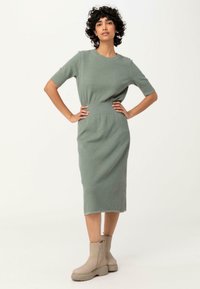 Abito midi in maglia di un delicato verde con maniche corte e una vita a coste, abbinato a stivaletti beige alla caviglia con suola spessa.