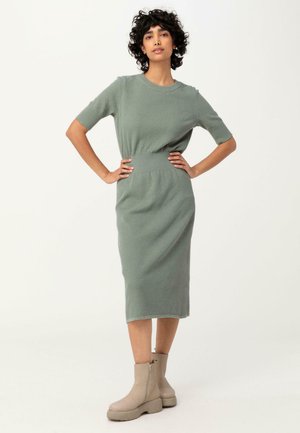Robe midi en tricot vert doux avec des manches courtes et une ceinture côtelée, associée à des bottines beige à bout carré avec une semelle épaisse.