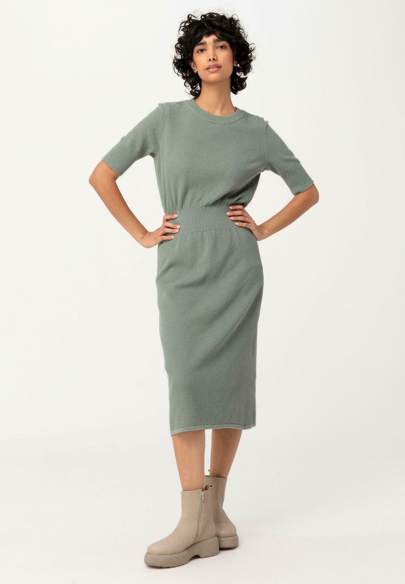 Abito midi in maglia di un delicato verde con maniche corte e una vita a coste, abbinato a stivaletti beige alla caviglia con suola spessa.
