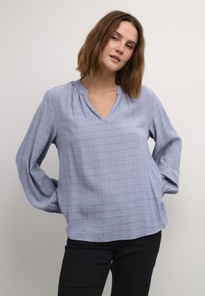 Light blue long-sleeve blouse with a v-neckline, gathered detailing at the collar, and a textured fabric featuring a check pattern.