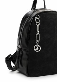 Sac à dos noir texturé avec fermeture éclair argentée et chaîne comportant un pendentif circulaire avec le logo SF suspendu à l'avant.