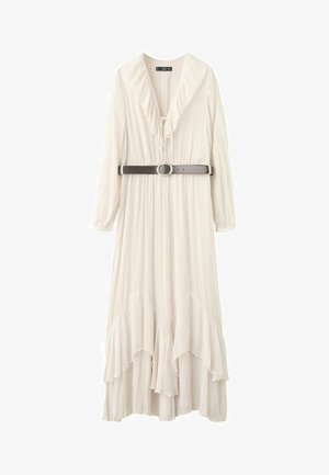 Longue robe blanche avec col en V à volants, manches longues, ourlet asymétrique, et ceinture noire avec boucle ovale argentée à la taille.