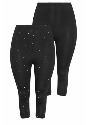 Kvinde går iført oversize hvid T-shirt, sorte korte leggings med hvide polkaprikker og hvide sneakers på lys baggrund.