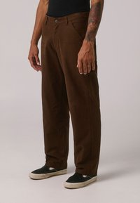 Brune kordfløjspant med lige ben-design, der har forlommer og metalknaplukning, parret med sorte slip-on sko.