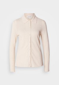Chemise crème à manches longues avec col et boutons à l'avant, présentée sur un fond blanc uni. Aucun motif ni décoration visible.