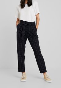 Czarne spodnie w kratę z paskiem w talii, o dopasowanym kroju. Do tego lekka krótka bluzka w kratę i trampki.