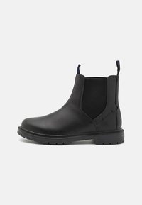 Botas Chelsea de cuero negro con paneles laterales elásticos, suela de goma gruesa y talón reforzado. Presenta tiradores para facilitar su uso.