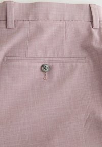 Poche arrière d'un pantalon en tissu rose texturé avec fermeture à bouton unique et passants pour ceinture à la taille.
